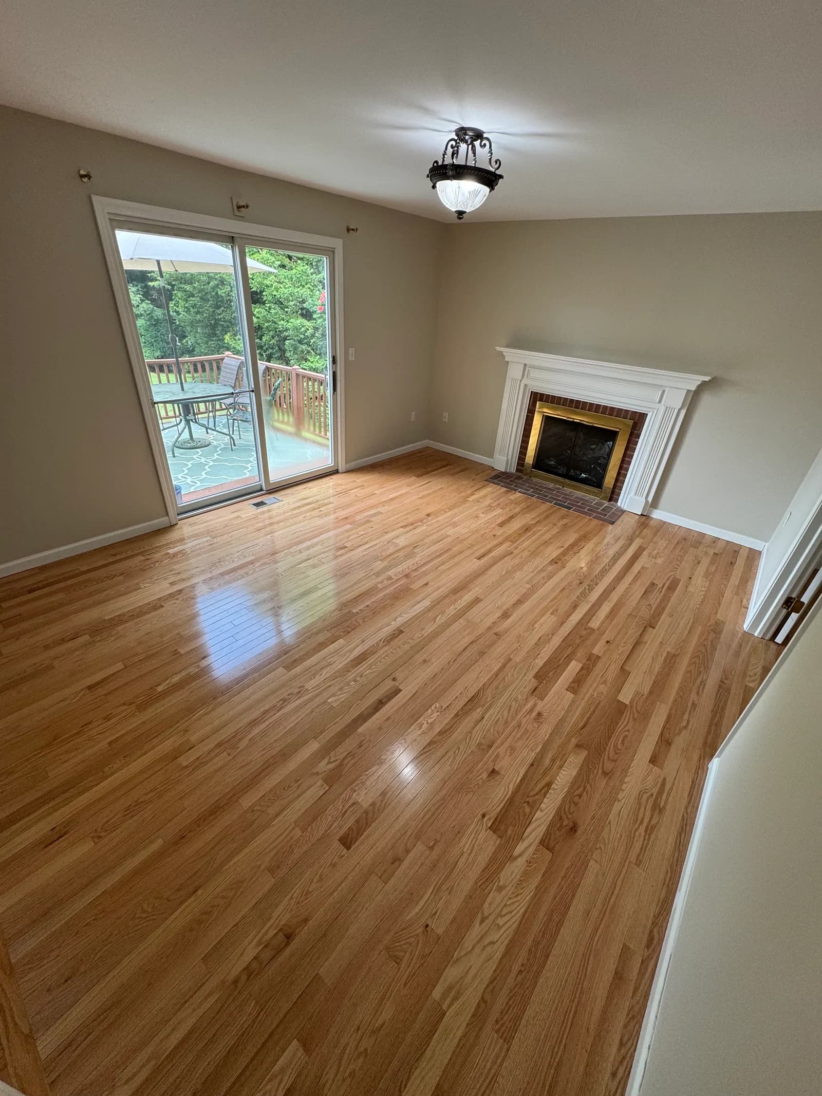 Hardwood flooring fitted around a brick fireplace and sliding patio door.